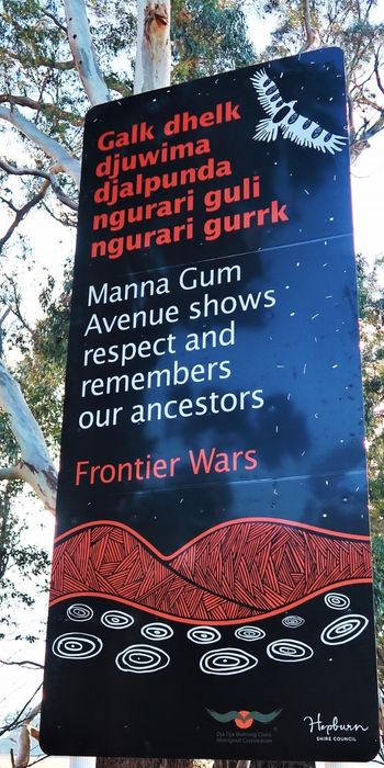 A large metal sign that reads 'Manna Gum Avenue shows respect and remembers our ancestors'. Beneath this is written 'Frontier Wars' and above is the same text in an Aboriginal language.