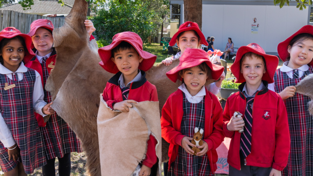 Schoolchildren in red uniforms, smiling at the camera, some of them wearing or showing off animal skins.