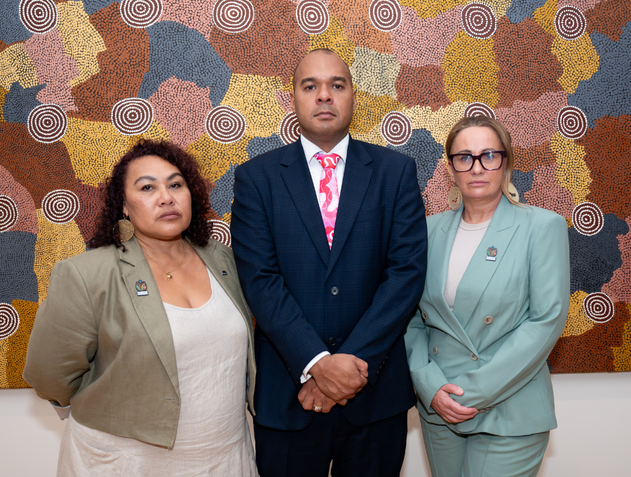 Three people standing in front of an artwork. Their expressions are firm. They are Karen Mundine, CEO of Reconciliation Australia: Joshua Creamer, Chair of the Queensland Truth-telling and Healing Inquiry; and Sue-Anne Hunter, Deputy Chair and Commissioner of the Yoorrook Justice Commission.