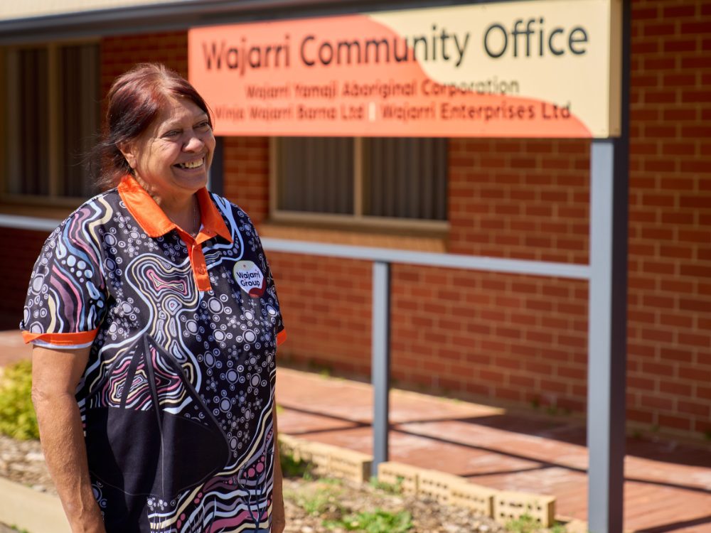 A woman stands, smiling, in front of the Wajarri Community Office.